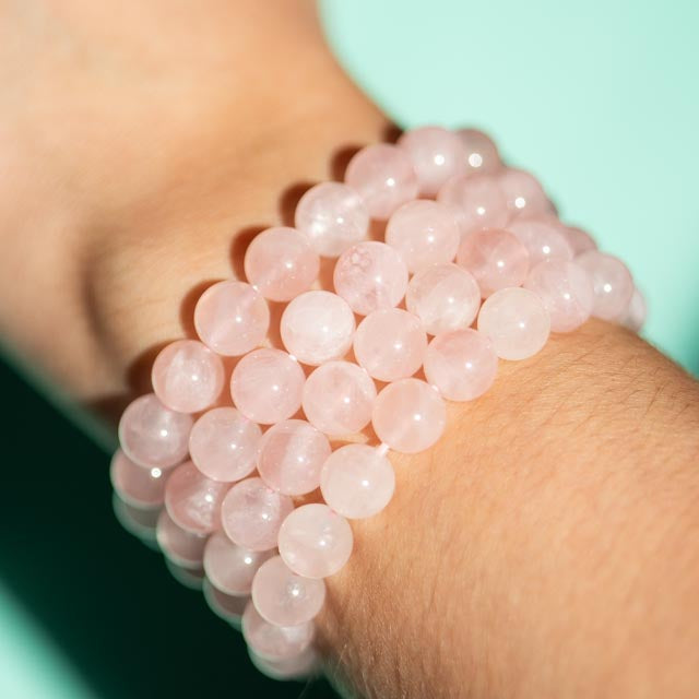Close-up of a wrist wearing a Rose quartz beaded bracelet against a light green background